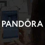 Miniatura de jogo em realidade aumentada da Pandora, exibindo logotipo branco centralizado sobre fundo escuro com smartphone em destaque.